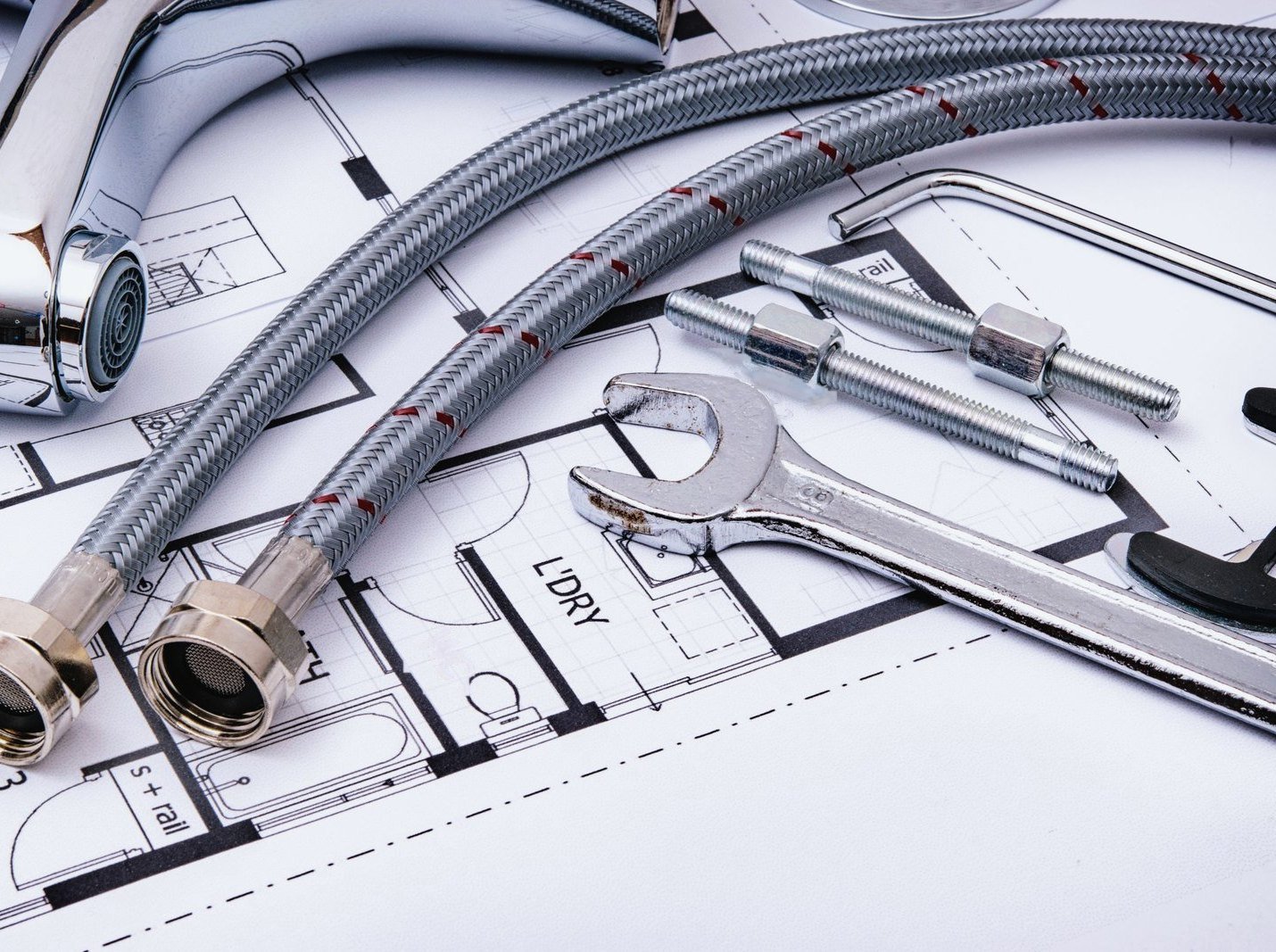 A faucet, braided supply lines, and wrenches laid over a house floor plan.