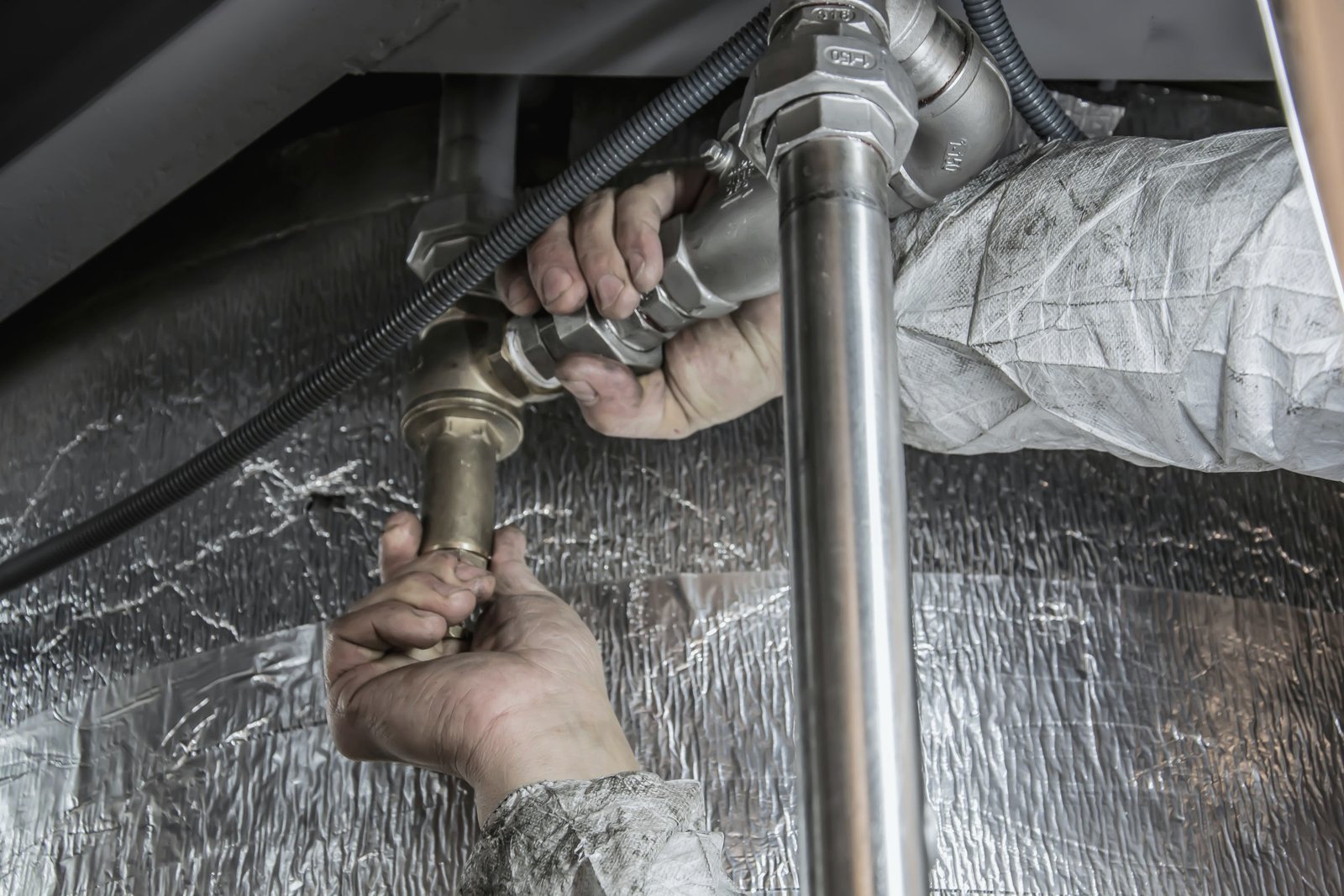 A plumber's hands tightening a brass valve assembly beneath a fixture.